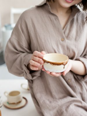 Woman smiling and holding a ceramic bowl created at pottery studio in beige earthy colors